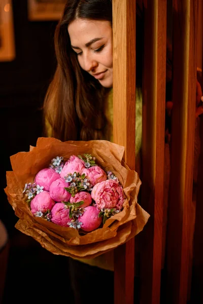 年轻美丽的黑发女子在木门附近摆设着华丽的粉红色牡丹花束 — 图库照片