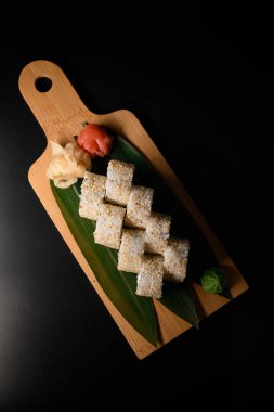 Tahta kesme tahtasındaki muz yaprağının üzerinde sunulan susam tohumlarıyla California Roll 'un en iyi manzarası. Zencefil ve wasabi yakınlarda. Siyah arka plan. Japon mutfağı kavramı.