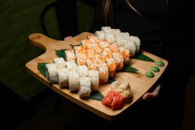 Kadınların el ele tutuşması, ahşap servis tahtasına yerleştirilmiş suşi rulolarının değişik çeşitleri ile yapılır. Siyah arka plan. Japon yenge kavramı