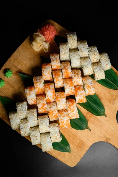 View from above on wooden serving board with different sets of california sushi rolls on black table background. Variety of japanese food. Restaraunt menu