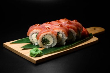 Salatalık, krem peynir ve muz yaprağı ve wasabi ile servis edilen teriyaki soslu Philadelphia ton balıklı suşi rulosunun iştah açıcı görüntüsü. Karanlık arka plan. Metin için boşluk