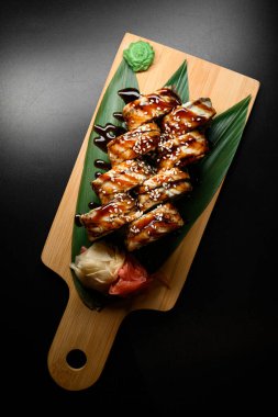 Tahta tahtada, bitki yaprakları, zencefil ve wasabi ile servis edilen teriyaki soslu füme yılan balığı suşisi rulosu. Üst Manzara. Japon yemeği..