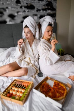 Bornozlu, şampanya bardaklı ve otelde yemek yiyen iki mutlu kadın eğlenerek vakit geçiriyorlar.