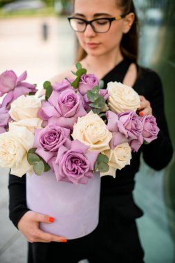 Seçici odak noktası menekşe buketi ve okaliptüs dallı kremalı güller genç çekici esmer kadınların elinde yuvarlak şapka kutusu. Düğün, doğum günü hediyesi.