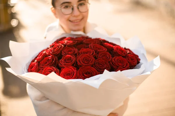 Big classy bright bouquet of red roses in hands of cute girl. One hundred and one roses in craft wrapping paper. Flowers shop concept