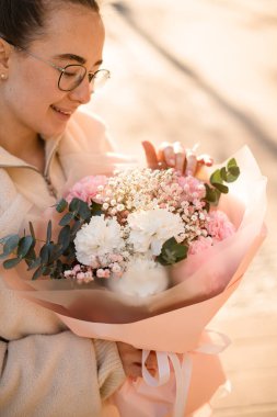 Gülümseyen esmer kız elinde güzel bir buket pembe ve beyaz karanfil ve paket kağıdında yeşil okaliptüs dalları tutuyor. Çiçekçi dükkanı konsepti. Dikey görünüm