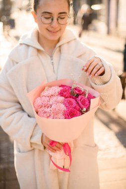 Çiçekçi logosuyla ambalaj kağıdına sarılı pembe güller ve karanfillerle dolu güzel bir buket tutan kadın. Taze buket. Çiçek teslimatı