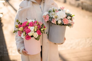 Elinde taze güller, Eustomalar, alstroemeryalar ve ellerinde şapka kutularında okaliptüs dalları olan iki çiçek buketi olan kadın. Arka plan bulanık. Ön görünüm
