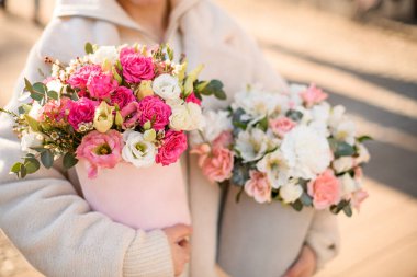 İki taze çiçek buketi içinde güller, Eustomalar, alstroemeryalar ve okaliptüs dalları açık havada kadınların elinde hediye kutularında. Arka plan bulanık. Çiçekçi. Çiçek teslimatı