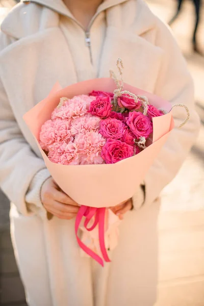 Woman holding pink beautiful bouquet of mixed flowers. Peony roses, carnations in wrapping paper. Flower shop. Flower delivery
