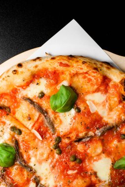 Ançüez, kapari, üzerine sarımsaklı cips ve taze fesleğen serpiştirilmiş mozarella peyniri serpiştirilmiş nefis Napoli pizzası. - Evet. Manzarayı kapat. Siyah arkaplan.