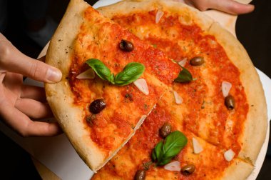 Şefin elindeki bir parça taze İtalyan pizzasının seçici odak noktası. Marinara soslu pizza, sarımsak cipsi, zeytin, taze fesleğen yaprağı ve kuru otlar..