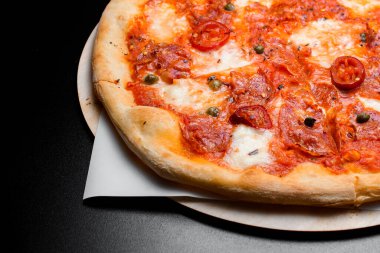 Tahta servis tahtasının üzerinde pepperonili ve kırmızı biberli taze pişmiş Meksika pizzasına yakından bakın. Siyah arka plan. İtalyan ya da Meksika yemeği yengesi