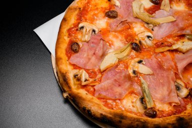 Tahta tahtada servis edilen mantarlı, jambonlu, domates soslu, zeytinli ve mozarellalı lezzetli pizza. Siyah arka plan. Restoran menüsü fotoğrafı.