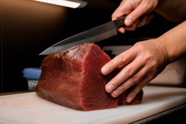 Şef, restoranın mutfağında tezgahta Japon bıçağı kullanarak taze ve çiğ ton balığı filetosunu ustaca kesiyor. Japon yemeği. Restoranda satılmak üzere Akami Tuna Sashimi..