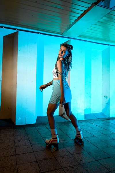 stock image Young woman wearing comfortable sport clothes and roller skates posing in underground passage. Backlited background. Healthy lifestyle