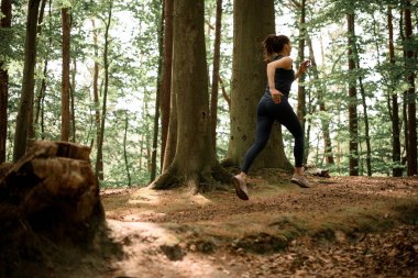 Siyah spor uiform giysiler giymiş, ağaç kütüğünün yanındaki ormanda koşan beyaz kadın. Sağlıklı bir yaşam tarzı. Hareket hayattır.