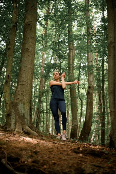 Atletik genç kadın orman patikasındaki günlük antrenmanından önce ısınıyor. Koşucu eğitimi, sağlıklı yaşam tarzı konsepti..
