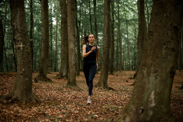 Young female athlete runs every day in forest, preparing for marathon. Runner training outdoors, healthy lifestyle concept.