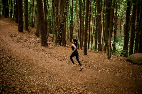 Female athlete running uphill on forest path in summer. Sporty woman working out running uphill. Runner training outdoors, healthy lifestyle concept.