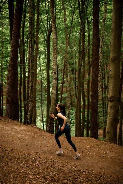 Woman runner running uphill on forest path in summer. Sporty woman working out running uphill. Runner training outdoors, healthy lifestyle concept.