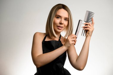 Beyaz arka planda profesyonel tarakları ve metin için fotokopi alanı olan çekici sarışın kuaförün stüdyo fotoğrafı. Ellerindeki saç taraklarının çeşitliliği. Kuaför salonu konsepti