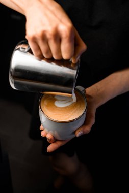 Kadın baristanın kalp siluetini çizerken metalik sürahiden kahve bardağına süt dökerken çekilmiş bir fotoğrafı. Kahve yapan bir bayan barista. Kahve sanatı