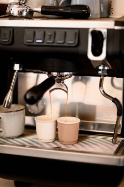 Kahve dükkanında ya da kafede kahve makinesinden alınmış iki küçük beyaz fincana koyu kahve dolduruyorum. Reklam pankartı. Kahve menüsü