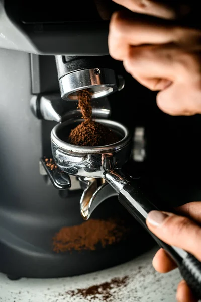 Female barista grinding coffee on professional grinder machine in coffee house closeup. Skilled young barista working in cafe with professional coffee machine