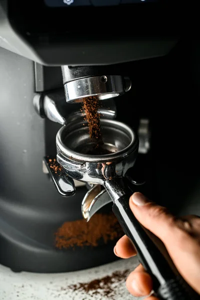 Female barista grinding coffee using professional grinder machine in coffee house, closeup view. Skilled young barista working in cafe with professional coffee machine