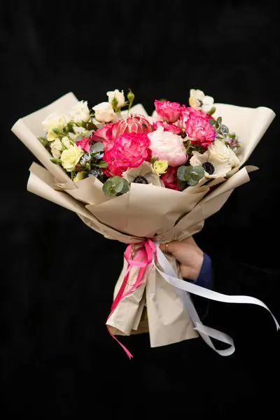 Black isolated flower bouquet wrapped in craft paper and white and pink satin ribbon for valentine or wedding. Natural flowers on black background. Image with selective focus and with copy space.