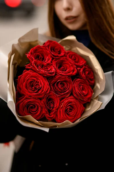 Selective focus of large bouquet with red roses for Valentines Day wrapped in brown paper. Woman with flowers bouquet. Blurred background