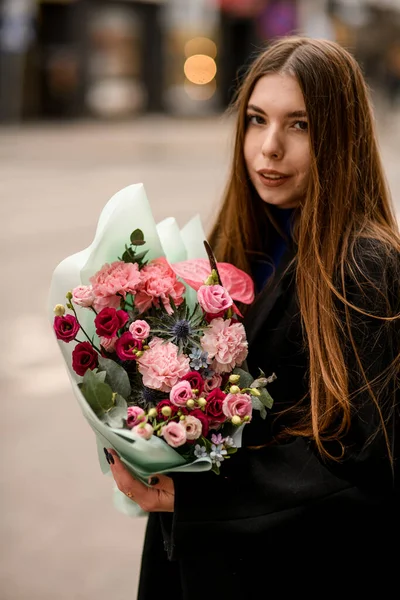 Young woman holding delicate flower bouquet of eustoma, carnations, anthurium and eucalyptus in red and pink colors. Beautiful bouquet of fresh mixed flowers wrapped in mint color paper. Flower shop.