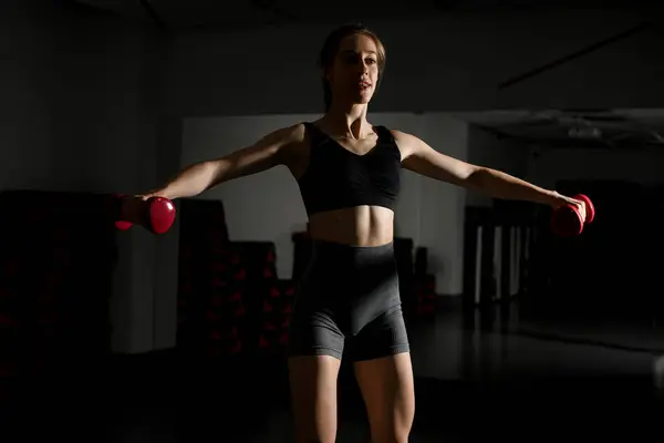 Attractive fit woman works out with dumbbells as a fitness conceptual over dark background. Athletic woman with perfect body. Strength and motivation