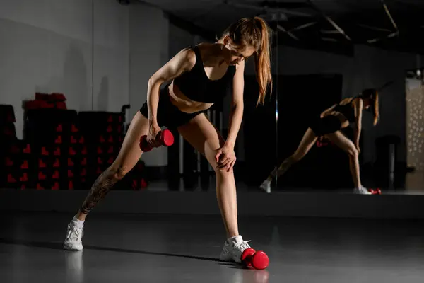 年轻体形苗条的女人在健身房里用红色哑铃在镜子背景下做手部肌肉运动 生活方式概念 — 图库照片