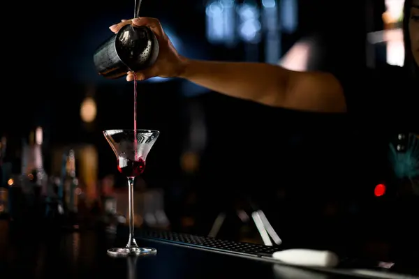 Woman bartenders hand pours liquid from shaker through cocktail strainer into cocktail glass at bar counter. Skillful girl bartender working in the bar