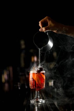 Barmen kızın elindeki manzara çok güzel. Çelik bardaktan bardağa buharlı sıvı dolduruyor. Kız barmen bar tezgahında portakal dilimleriyle sıcak içecek hazırlıyor.