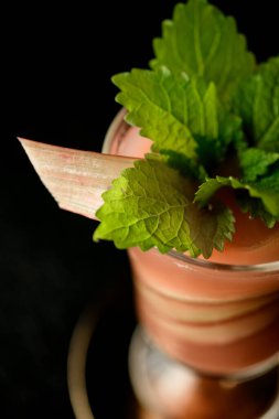Kırmızı çilek kokteyline yakından bakın. Siyah arka planda yüksek camlı nane yaprağı ile süslenmiş. Seçici odaklanma. Bar menüsü için çekim.