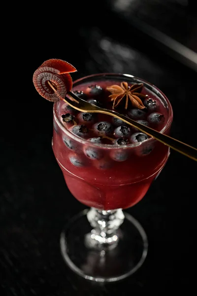 Glass with red hot alcoholic cocktail with blueberry and allspice, decorated with apple pastille. Top view, dark background