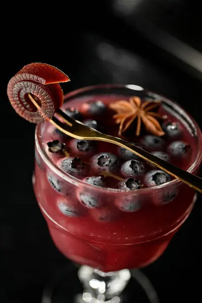 Glass with red alcoholic cocktail with blueberry and allspice, decorated with apple pastille. Top view, dark background