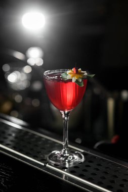 Karanlık arka planda saklanmış çiçekle süslenmiş içki bardağına alkollü kokteyl. Manzarayı kapat. Kokteyl menüsü için shot