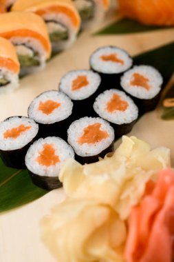 Ahşap tahtada çeşitli suşi ruloları izole edilmiş. Somon, kırmızı ve beyaz zencefil, wasabi, nigiri