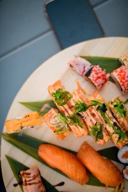 Gri bir masadaki ahşap tepside suşi ruloları, yanında da bir akıllı telefon var.