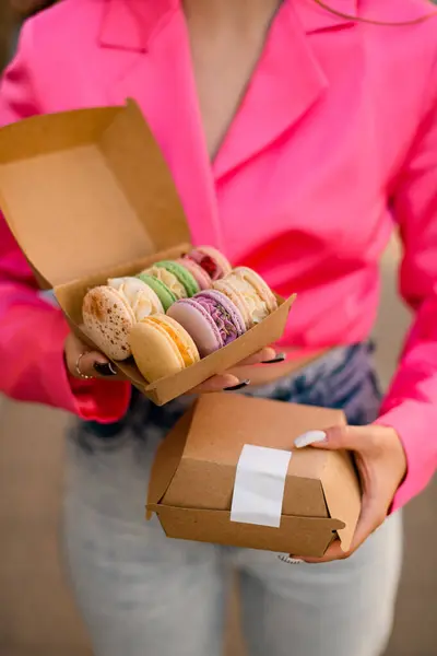 Female hands in a bright pink shirt holding two sets of colorful macaroons, delicious French Biscuits