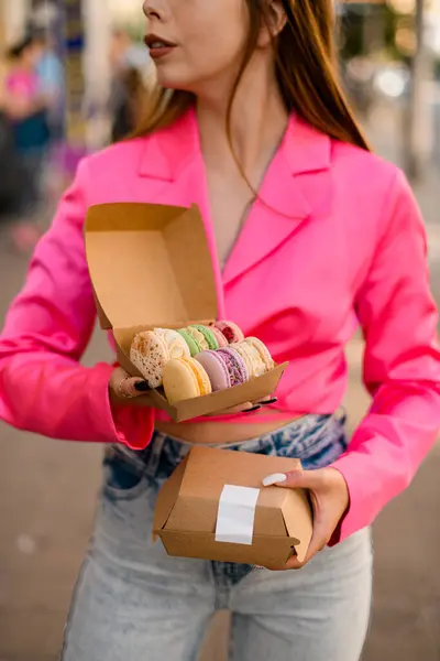 Pretty woman in a bright pink shirt holding two sets of colorful macaroons, delicious French Biscuits