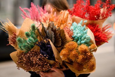 Kahverengi bir kağıdın içinde farklı buket kuru çiçek, güzel bir esmer kadının ellerinde.