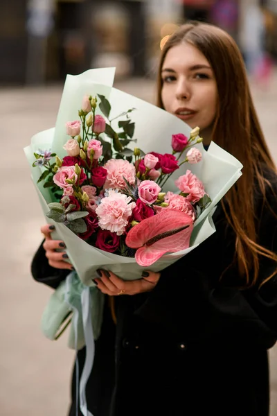 pretty woman in a black coat with a big bouquet of pink roses on a blurred street background