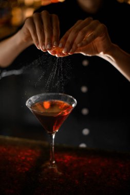 Kadın barmen elleri taze sıkılmış portakal kabuklarını kokteyl bardağına dolduruyor.