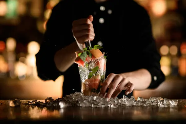 Female hands breaks ice in a glass with a drink using a mulder, splashes and pieces of ice and grapefruit flying to the sides