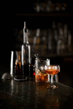 Barmen ekipmanları, hazır bir buzlu kokteyl ile karıştırma bardağı ve yarısı buz parçasıyla dolu bir kokteyl bardağı tezgahın üzerinde.